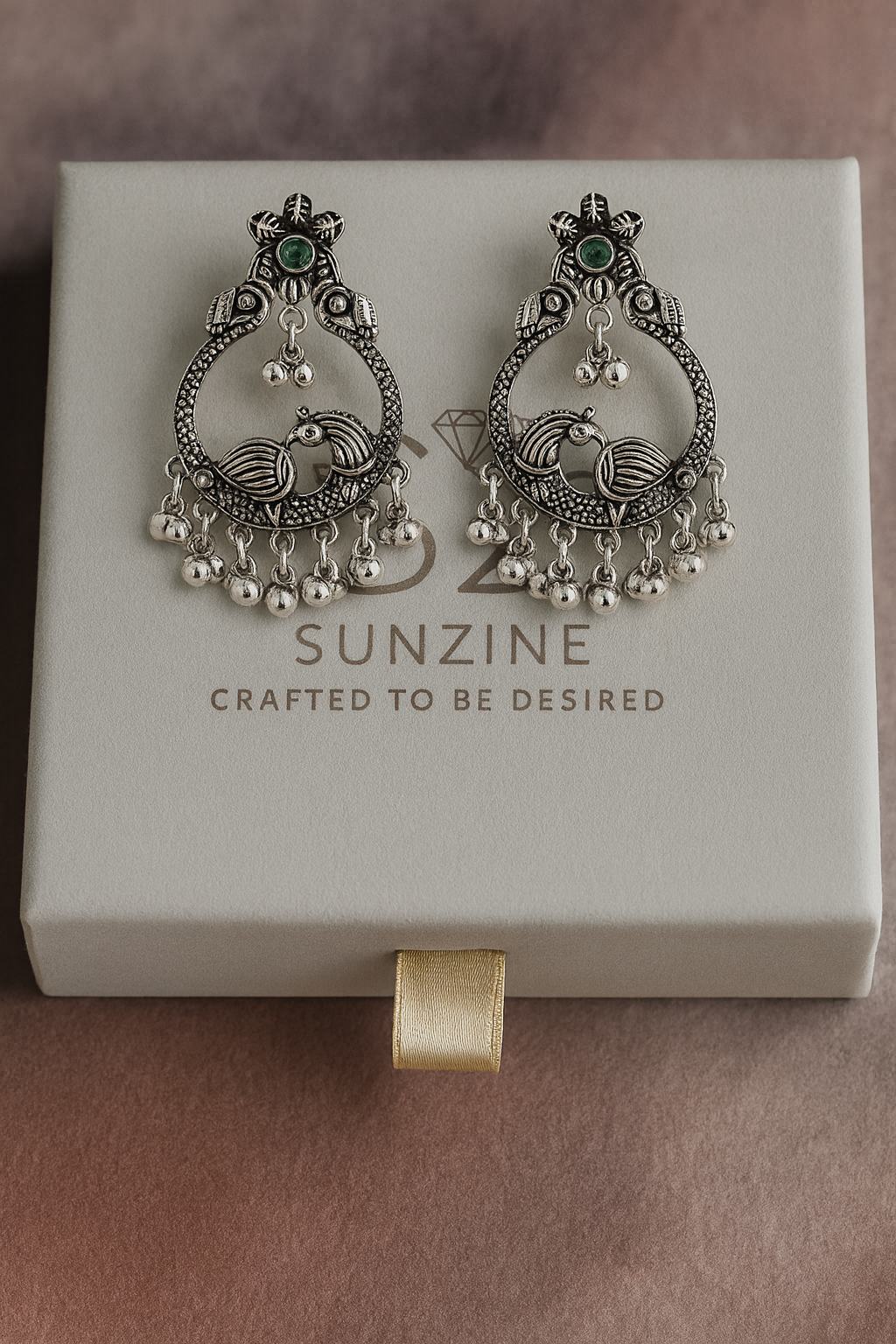 Ornate silver earrings with green gemstones on a Sunzine branded box.
